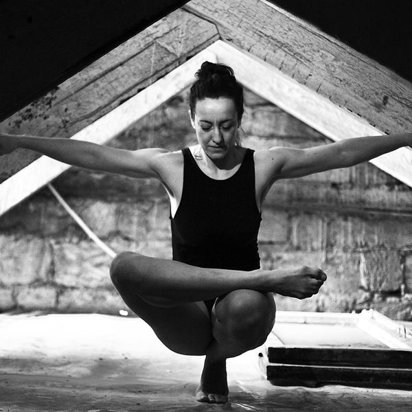 Woman in a peaceful yoga pose against a dark background with aquamarine light.